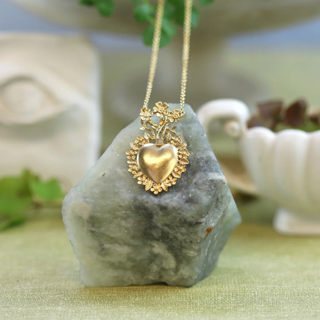 Alex Monroe gold heart locket necklace draped over a rock