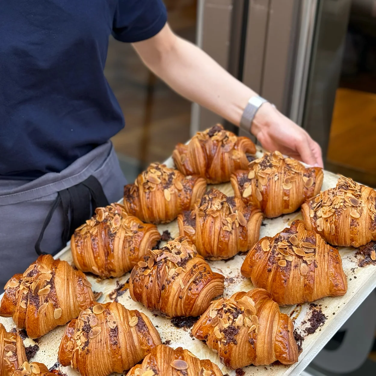 Arôme Bakery baker carrying a tray of almond croissants