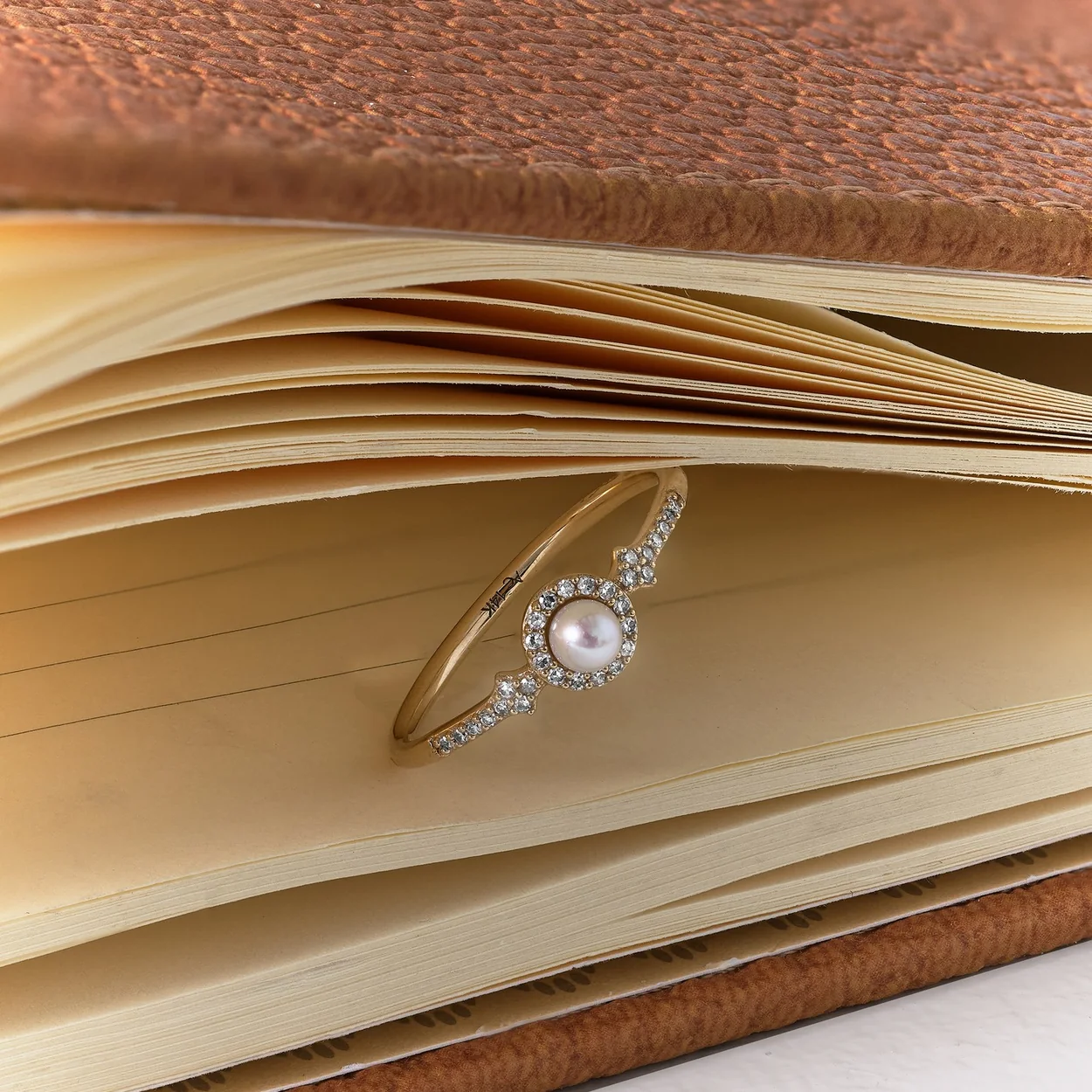 Astley Clarke pearl and diamond ring resting on a leather notebook