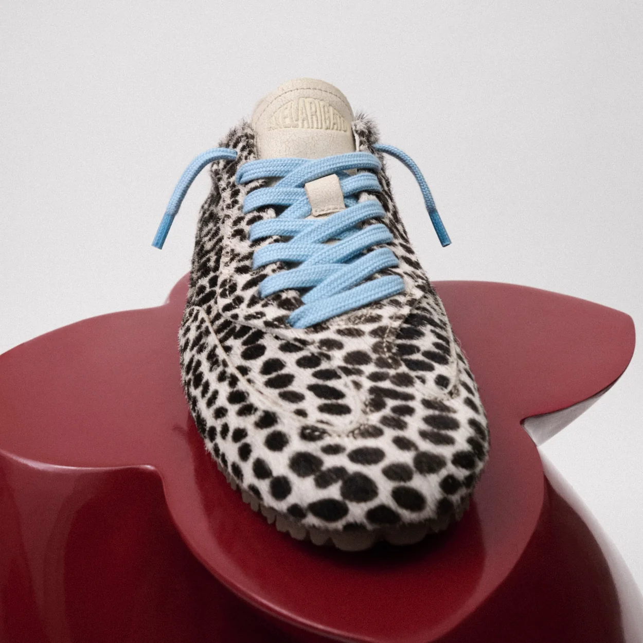 Axel Arigato animal-print trainer with blue laces on a red plinth