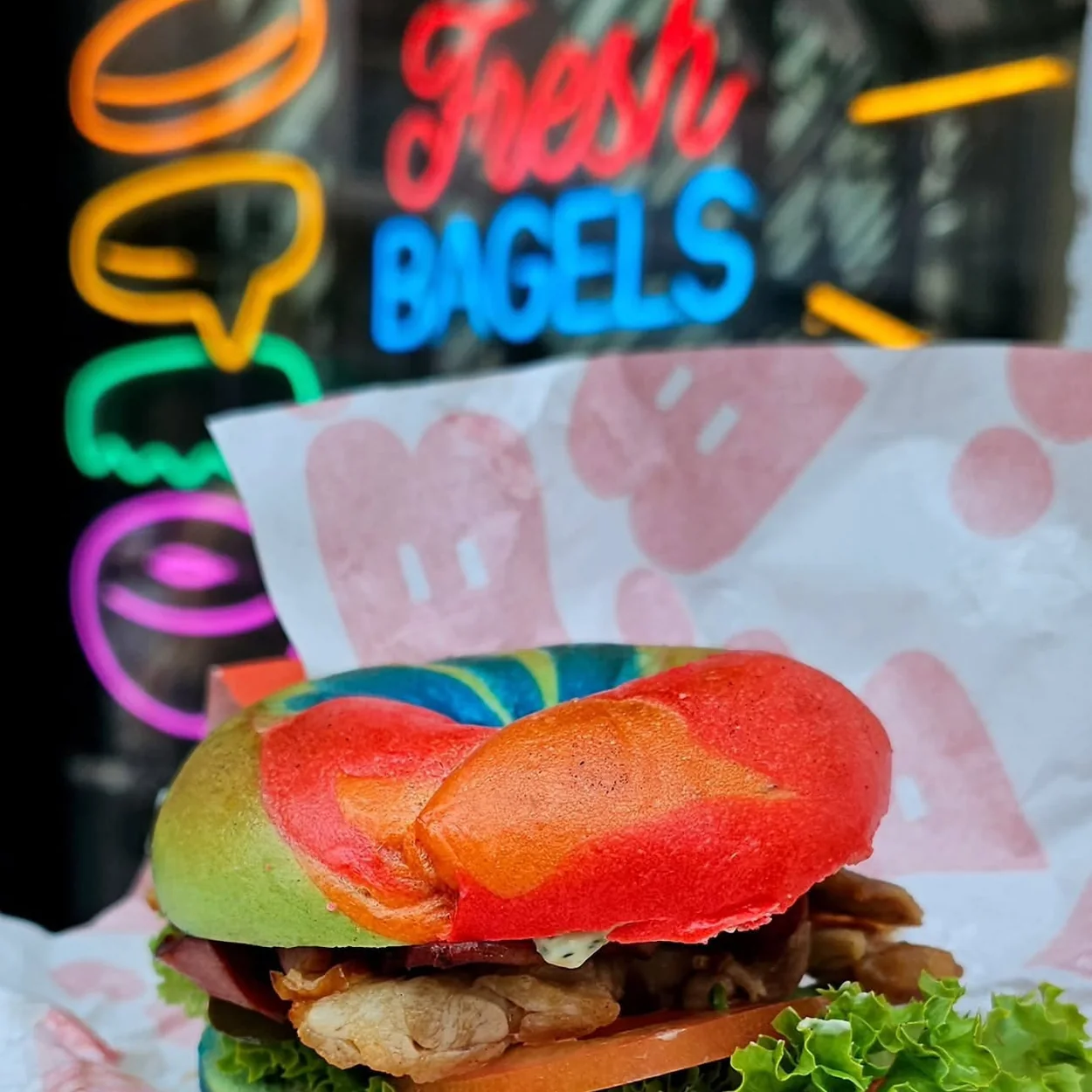 B Bagel filled rainbow bagel in front of the neon sign