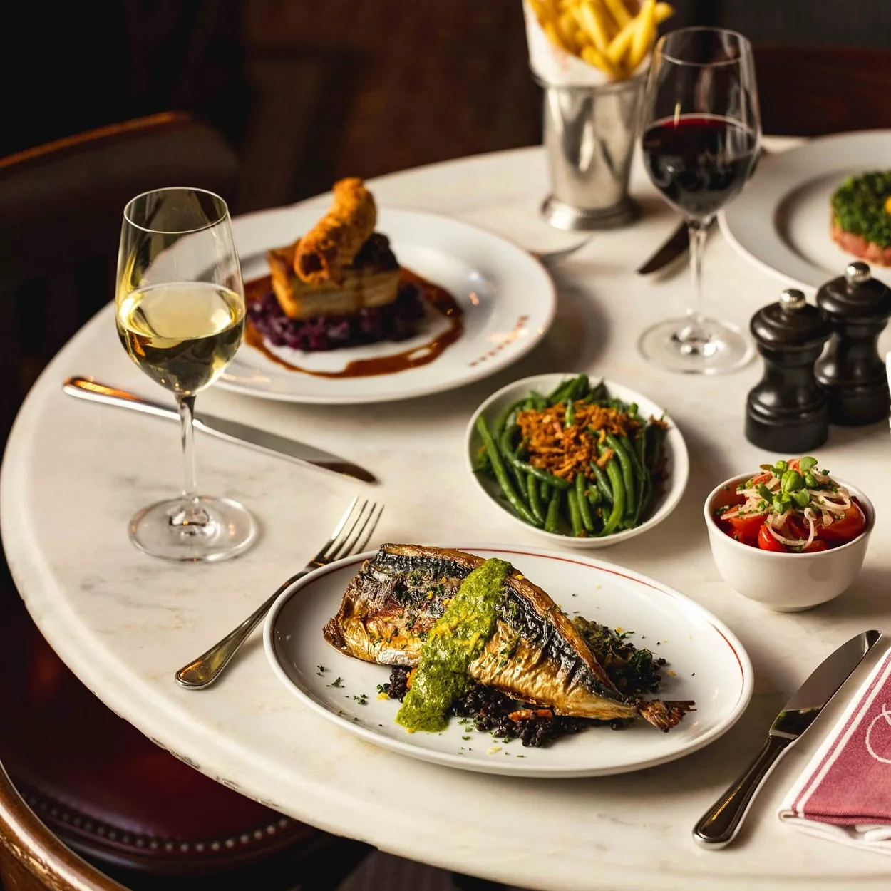 Balthazar table with grilled fish, chips, greens and red wine
