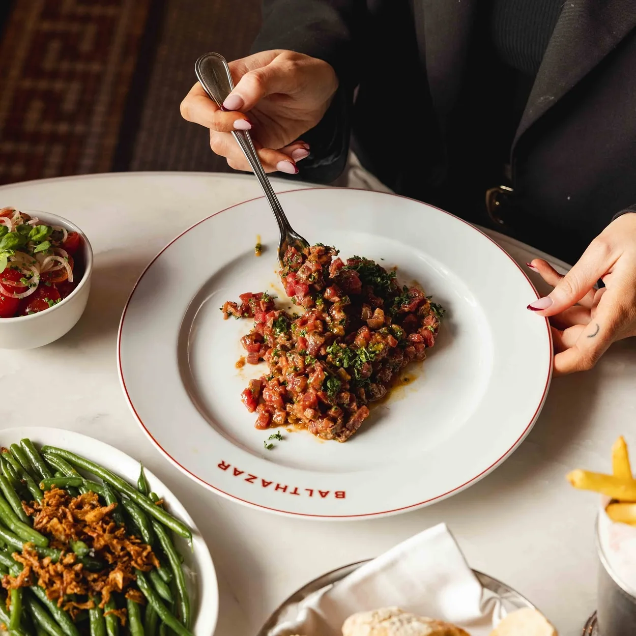 Balthazar diner mixing steak tartare at a marble table