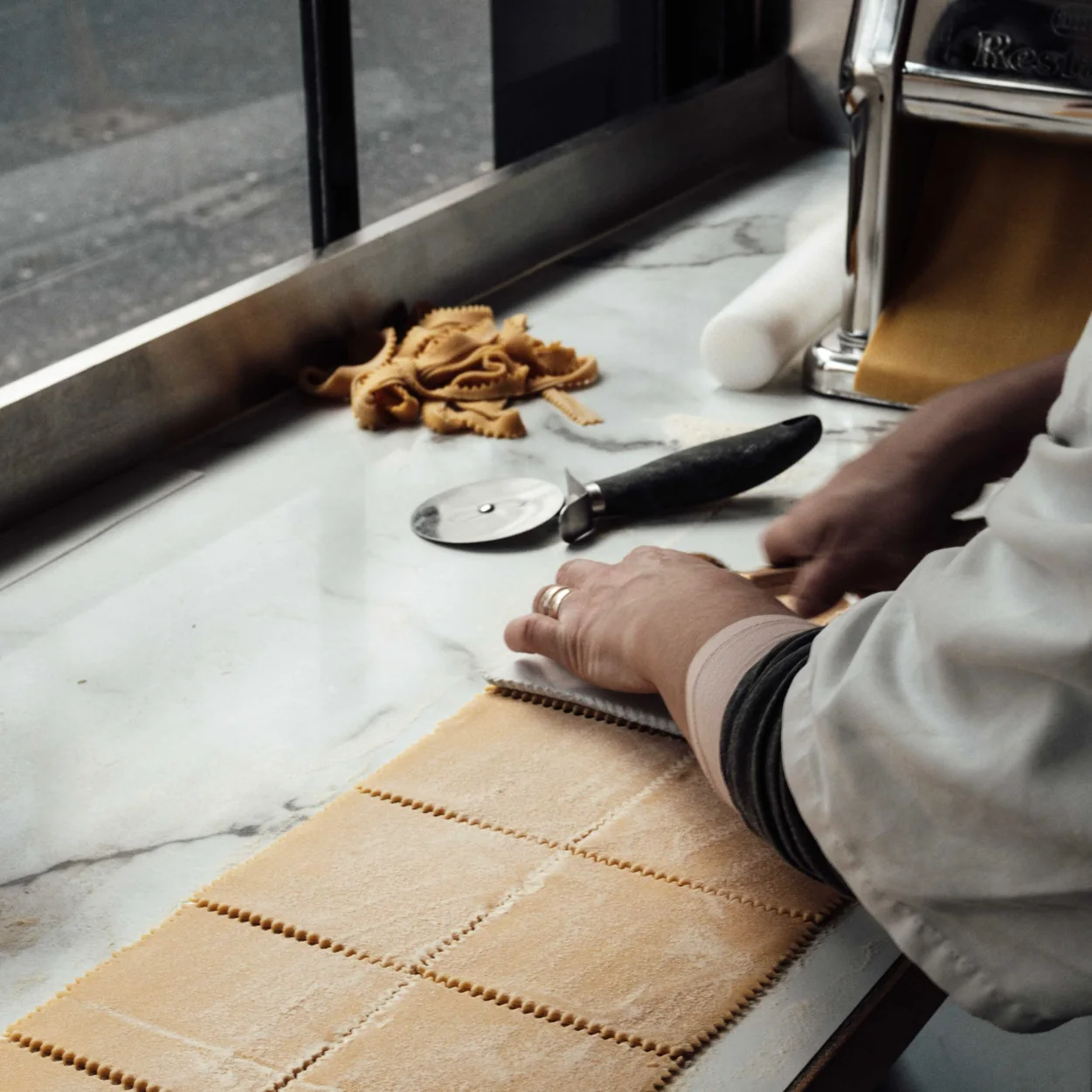 Bancone chef cutting fresh pasta sheets on the marble counter