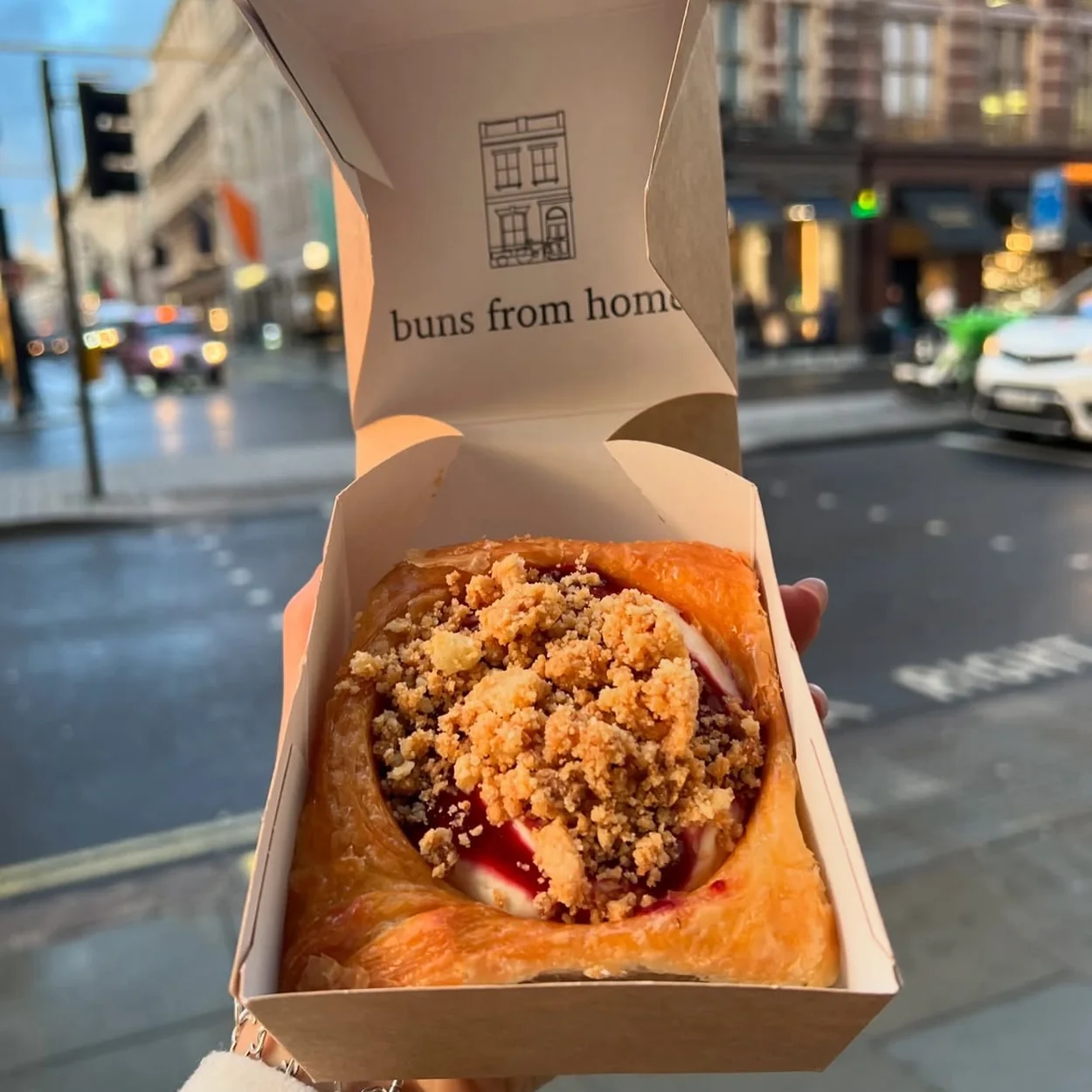 Buns From Home takeaway box with a crumble-topped bun on a London street