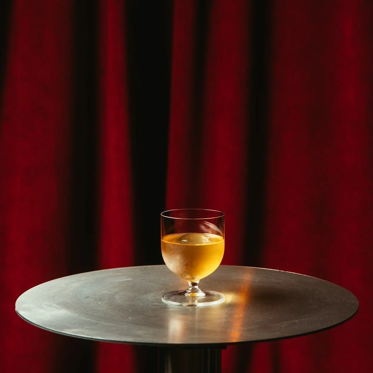Cato Covent Garden, a cocktail on a steel table against the red velvet curtain