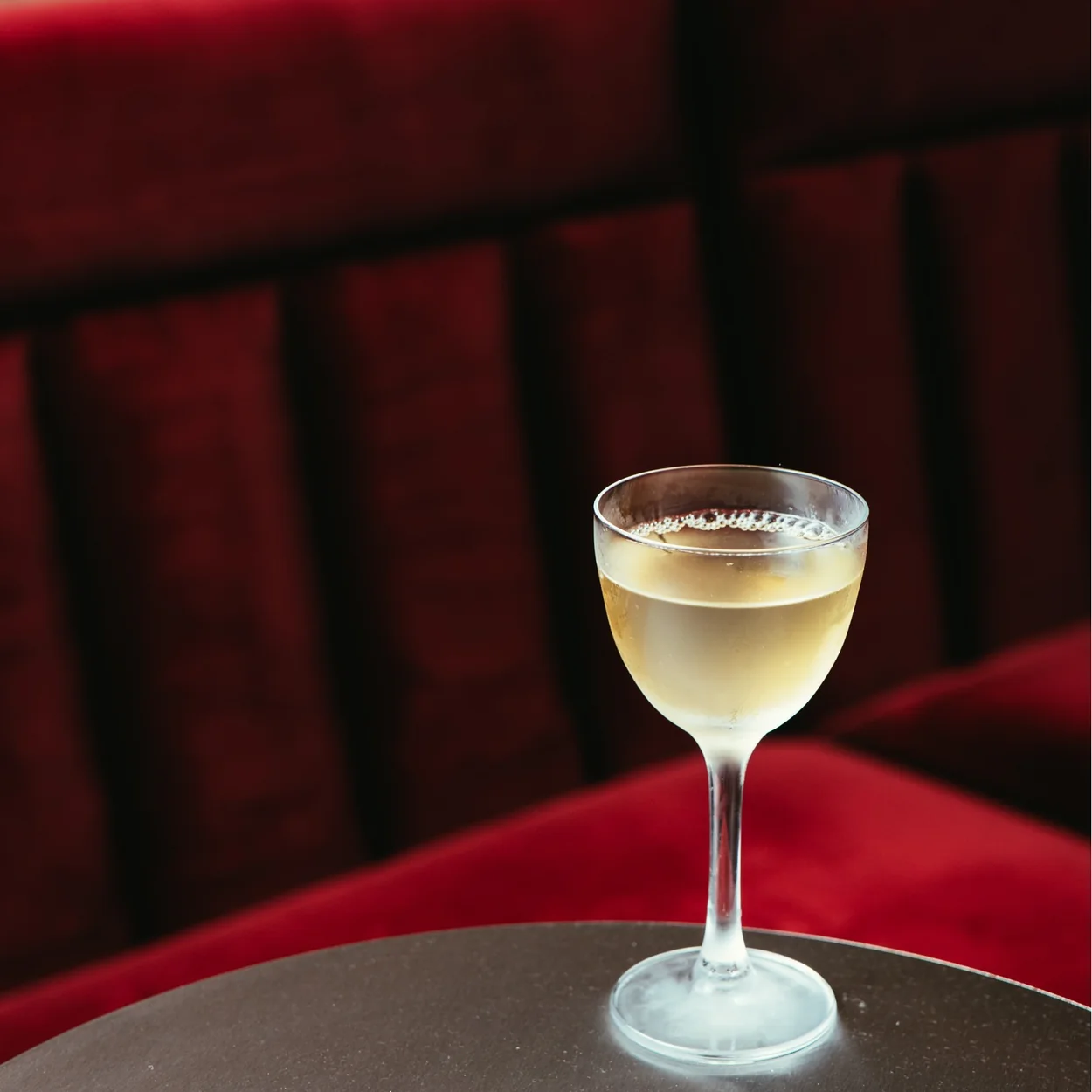 Cato Seven Dials, a chilled coupe cocktail beside the red velvet banquette