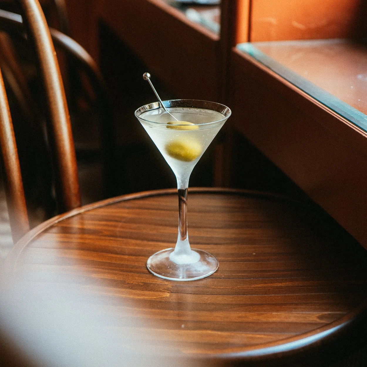 Cato martini with an olive on a wooden table by the window