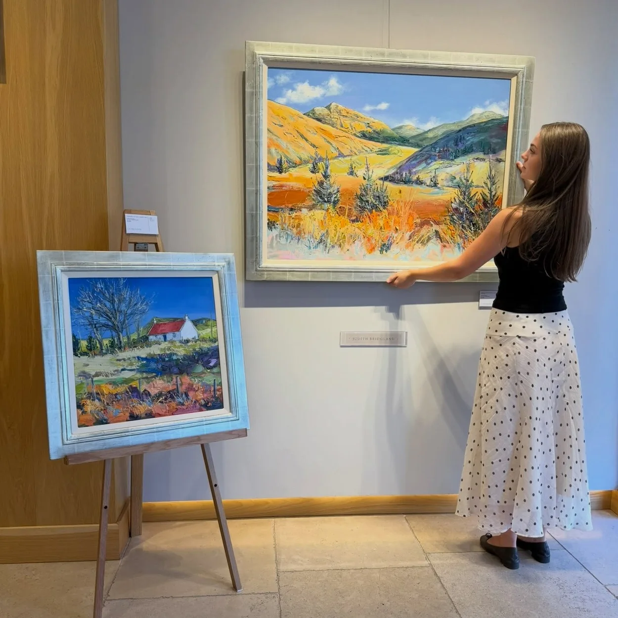Clarendon Fine Art consultant hanging a landscape painting beside an easel in the gallery