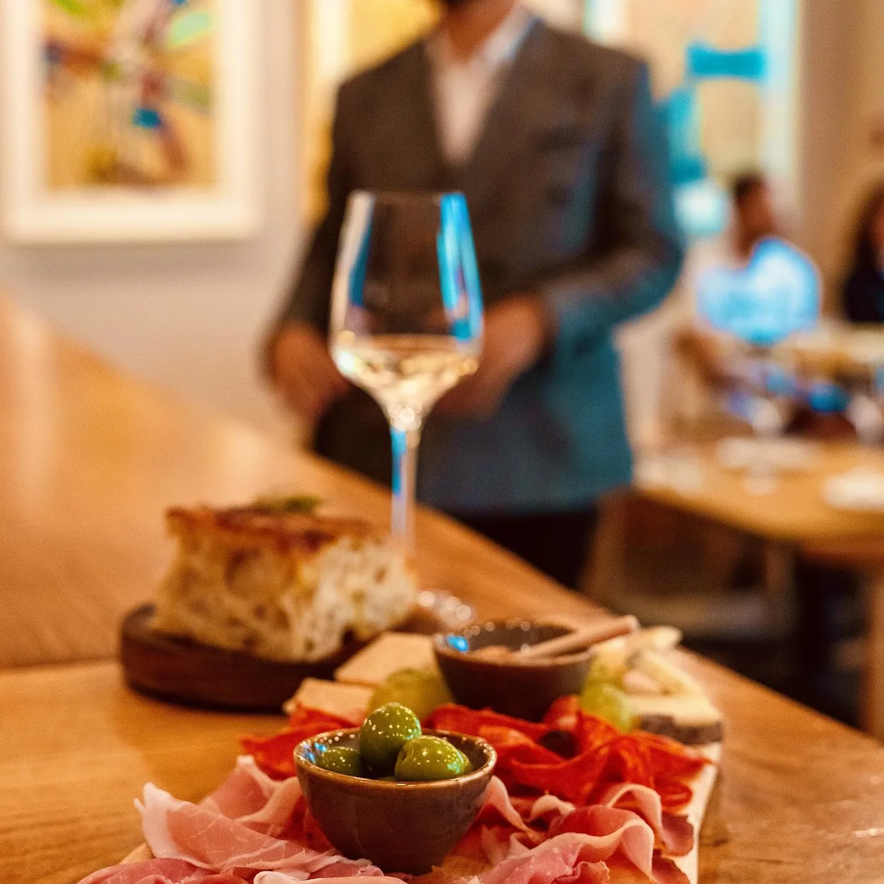 Dalla Terra antipasti board with cured meats, olives and a glass of white wine
