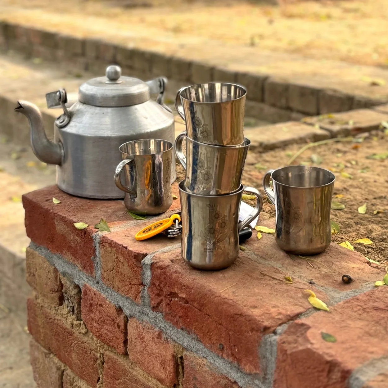 Dishoom chai kettle and steel cups on a brick wall