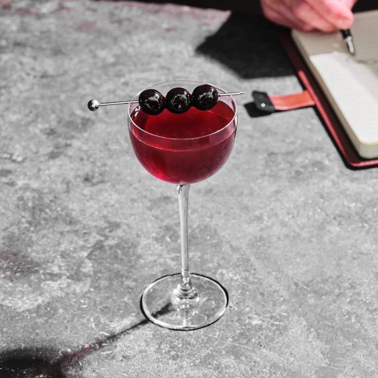 Eve Bar cocktail in a coupe garnished with dark cherries