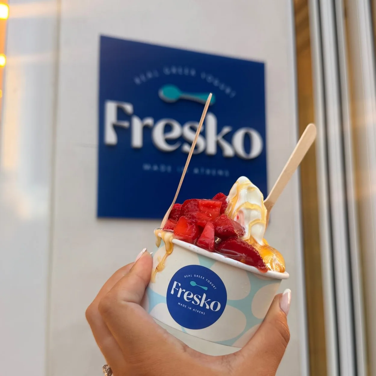 Fresko yogurt cup with strawberries held in front of the shop sign