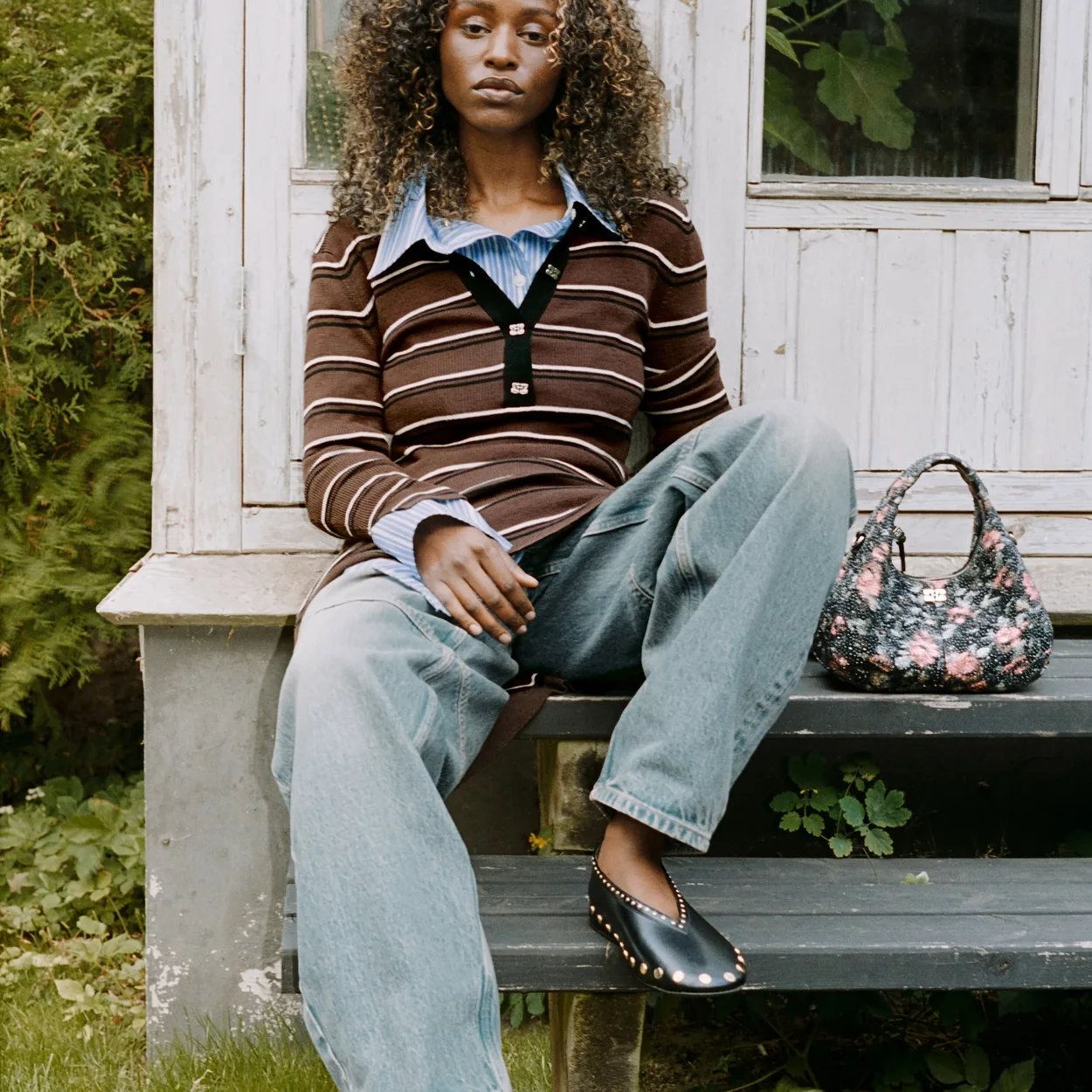 GANNI striped knit, wide denim and floral bag worn on a porch