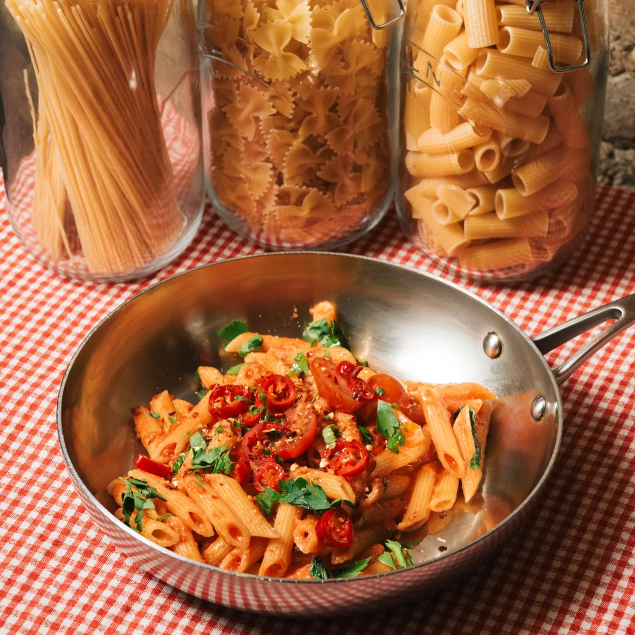 Guido's penne with tomato sauce in a pan beside jars of dried pasta