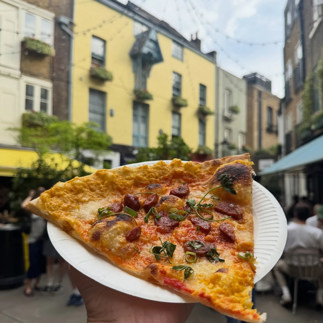 Homeslice slice on a paper plate held up in Neal's Yard
