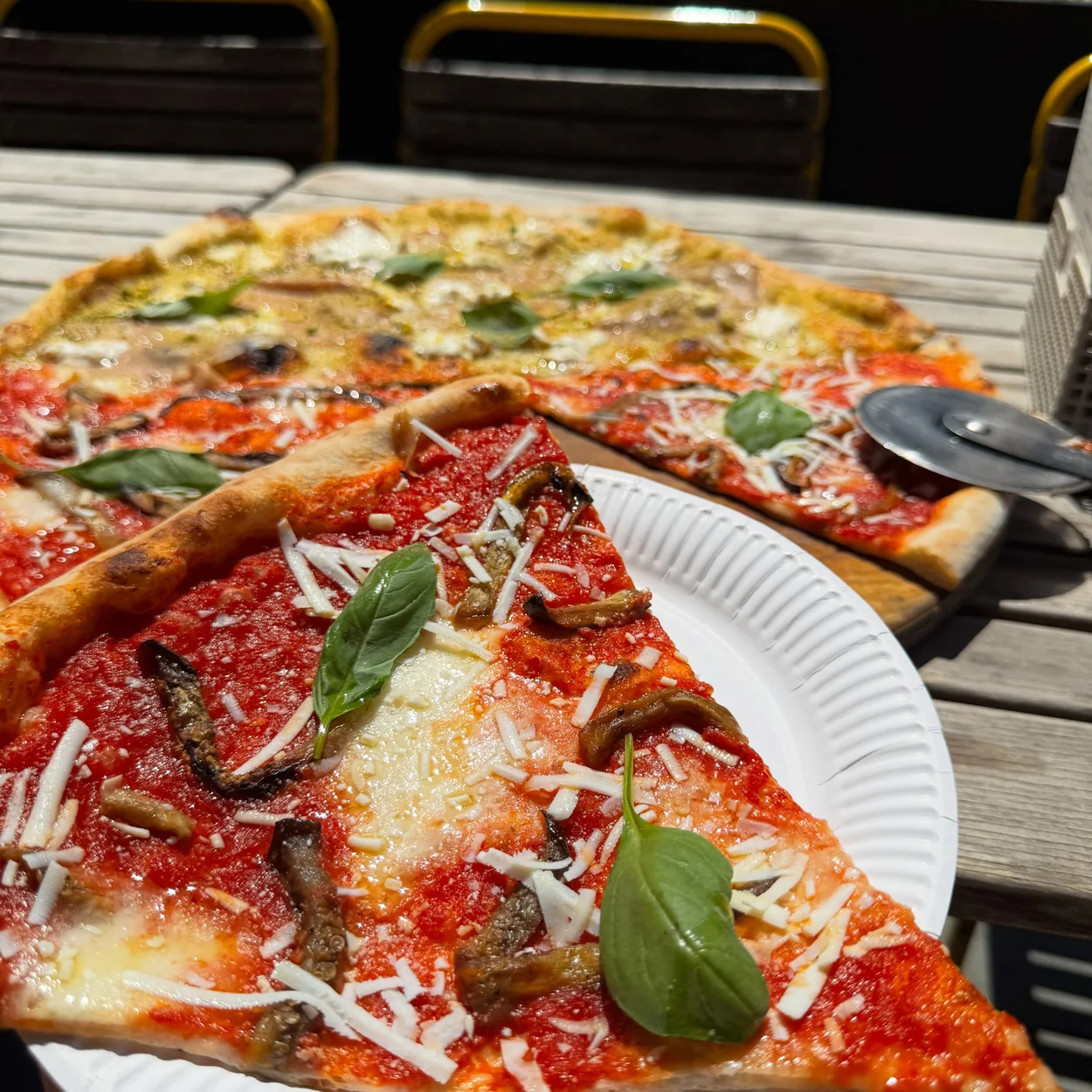 Homeslice pizza slices with basil and parmesan on paper plates