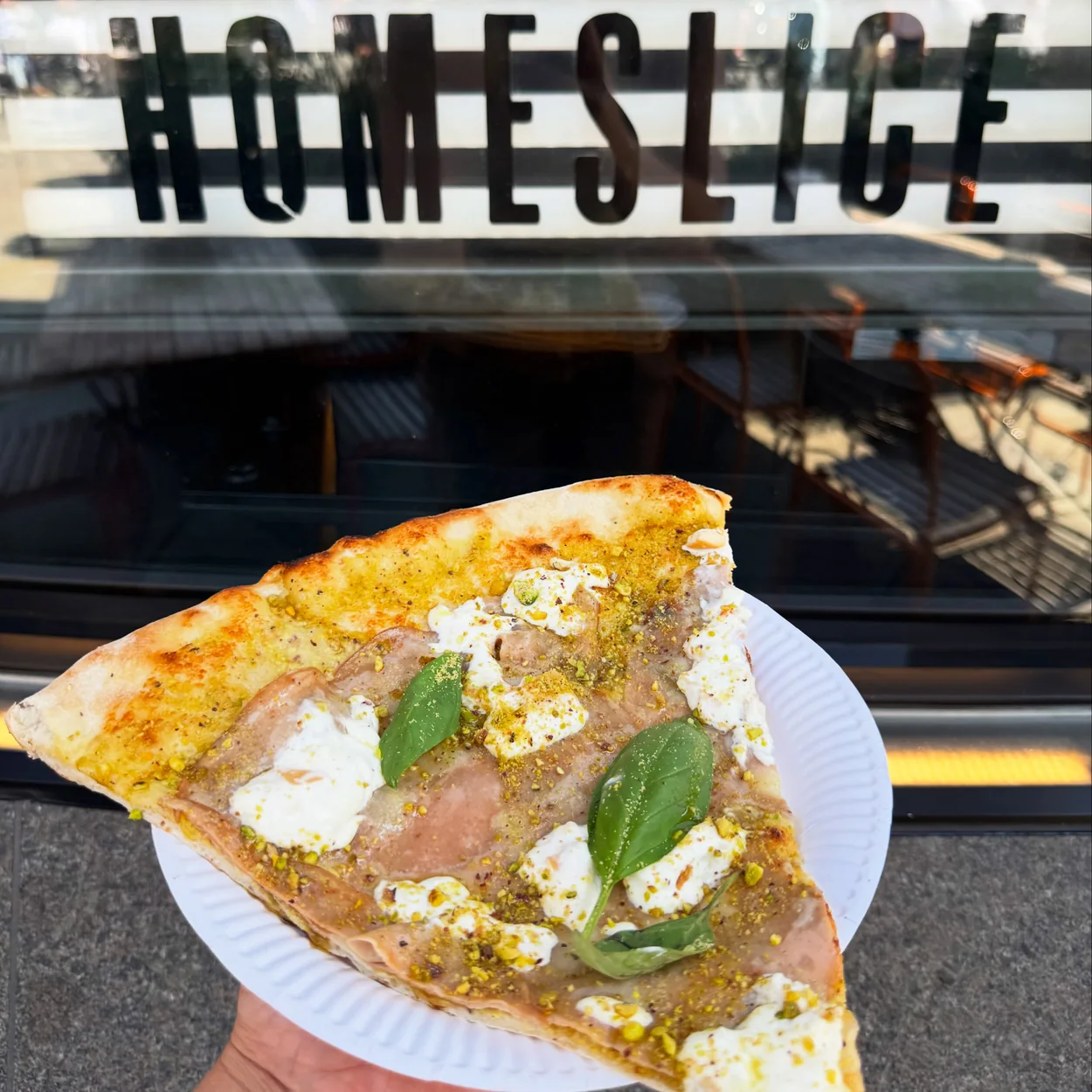 Homeslice pizza slice with ricotta held in front of the Neal's Yard shop sign