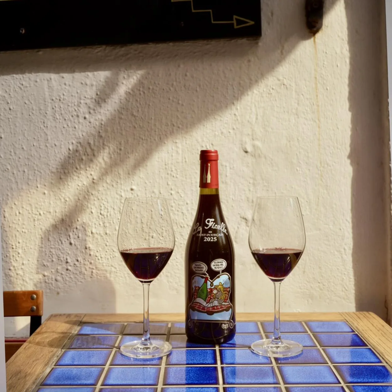 Le Beaujolais bottle of red wine and two glasses on a blue tiled table