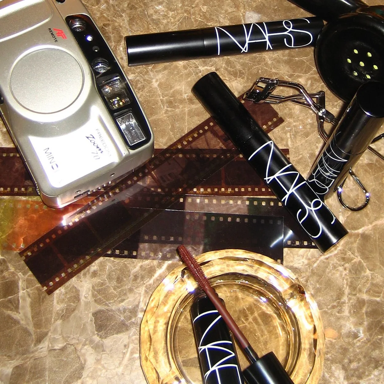 NARS mascara and eye pencils with a compact camera on marble