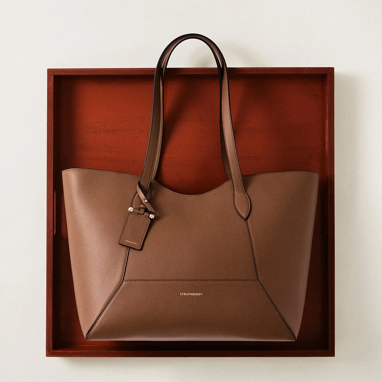 Strathberry taupe leather tote bag displayed in a wooden frame