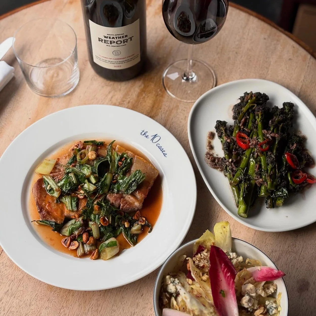 The 10 Cases sharing plates and a bottle of red wine on a wooden table
