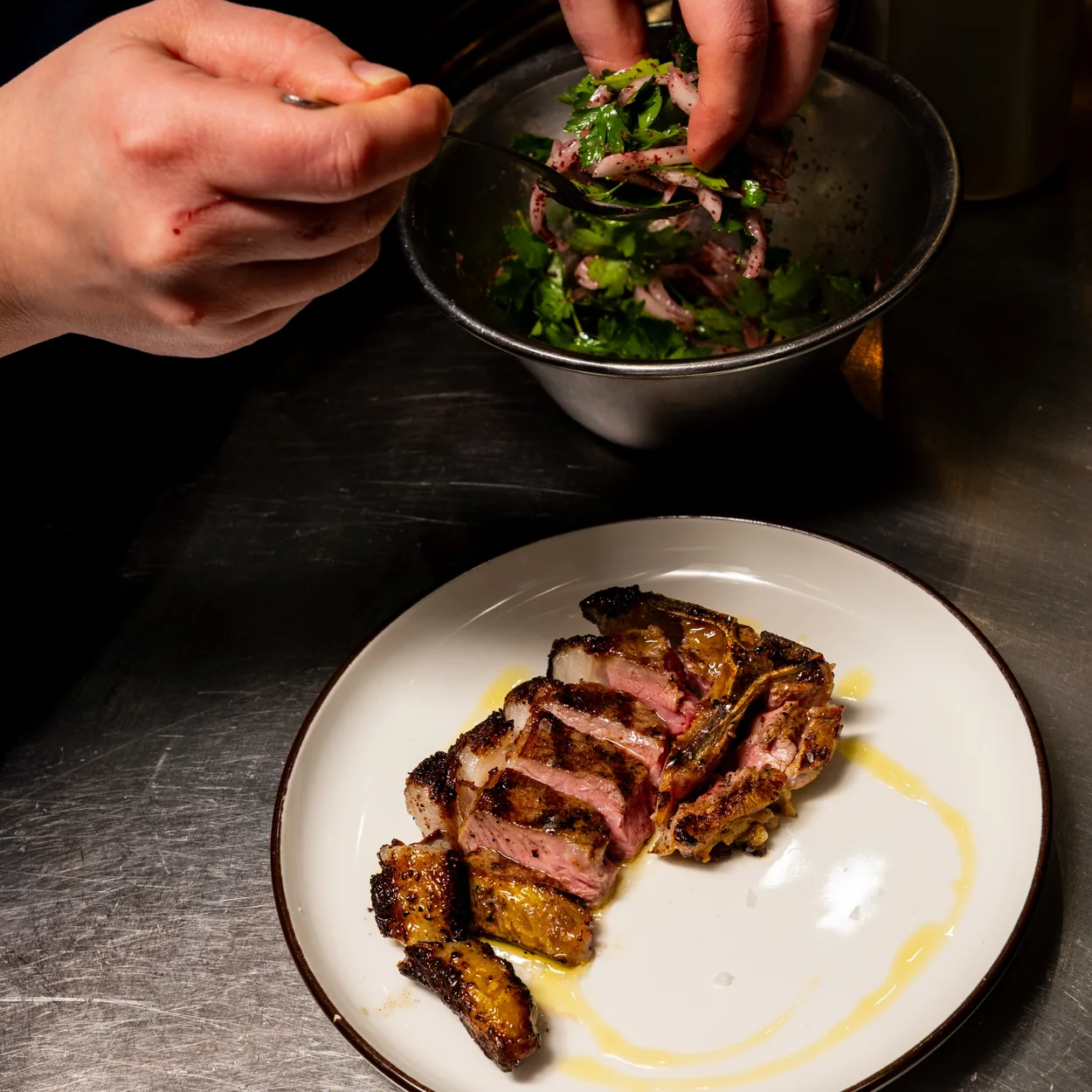 The Barbary chef plating sliced grilled meat with herb salad