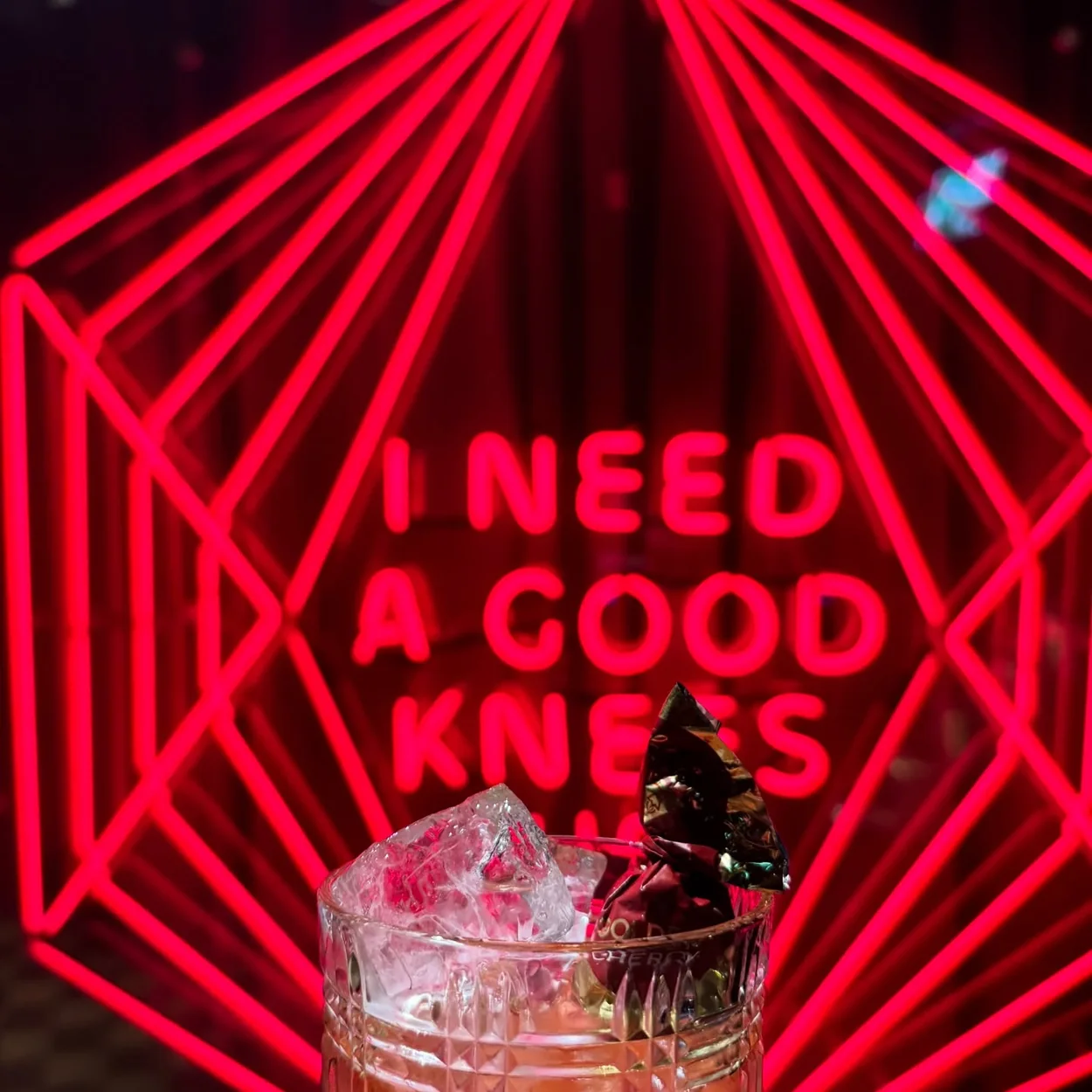 The Escapologist cocktail in front of the neon I Need A Good Knees sign