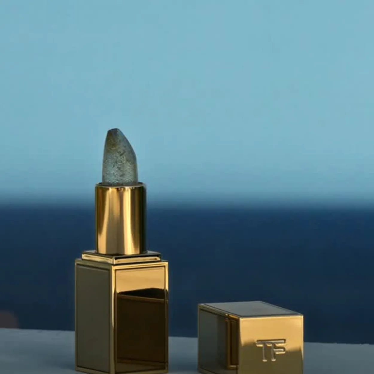 Tom Ford Beauty lipstick in a gold case against a sea backdrop