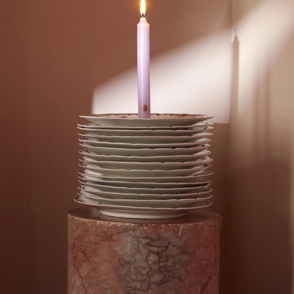 Trudon lilac taper candle on a stack of plates
