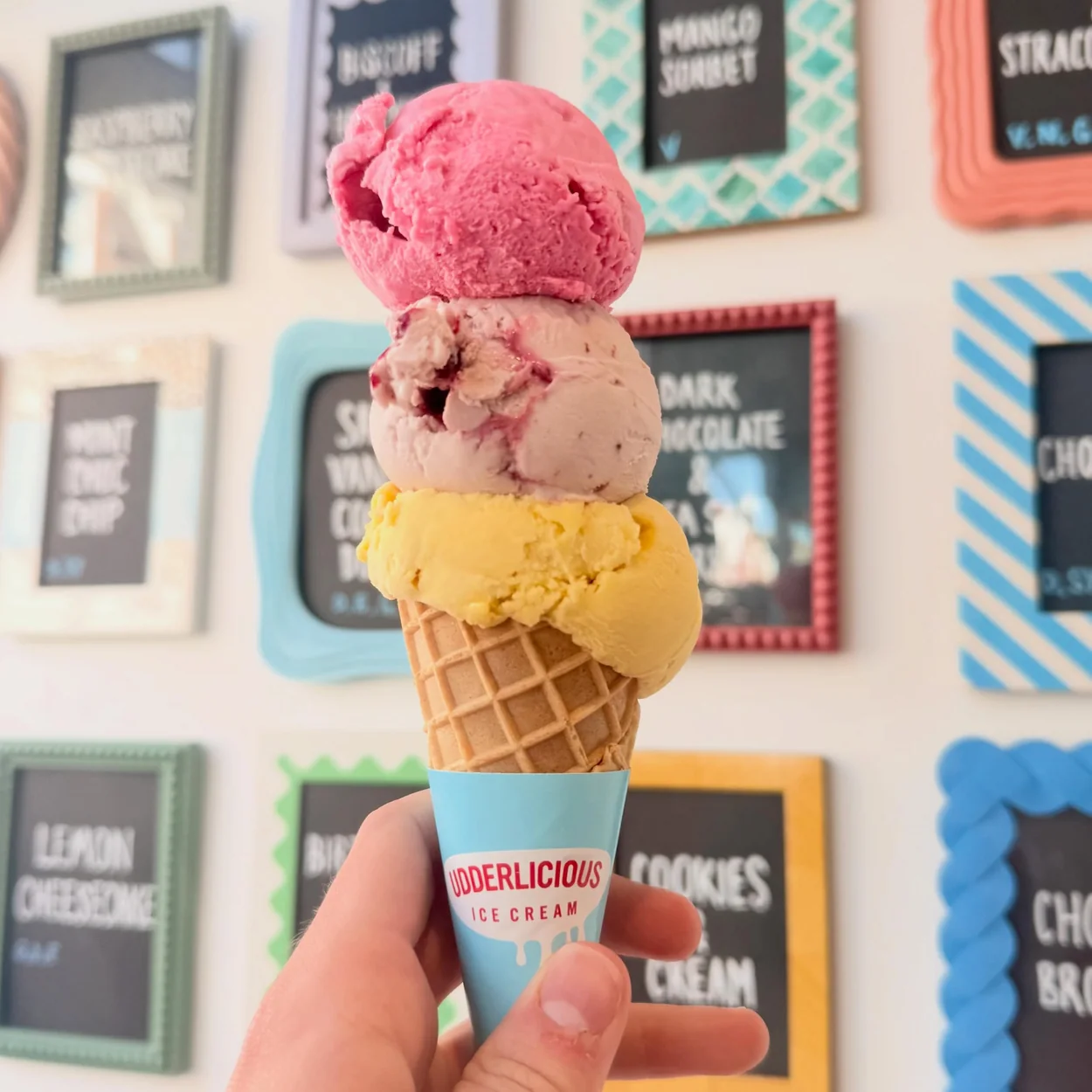 Udderlicious triple-scoop cone in front of the flavour board