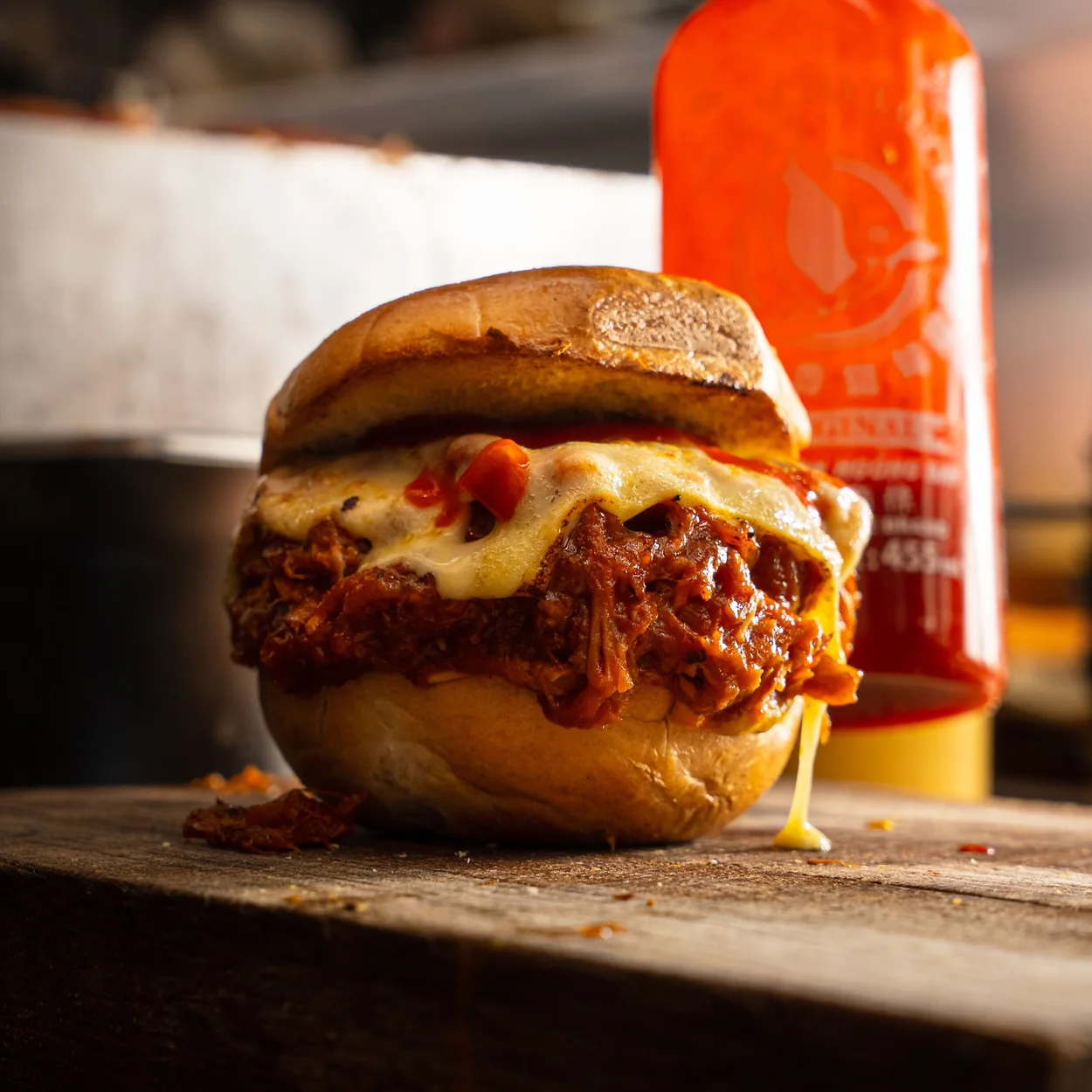 Filled bagel with melted cheese and hot sauce bottle behind at Dirty Bagels