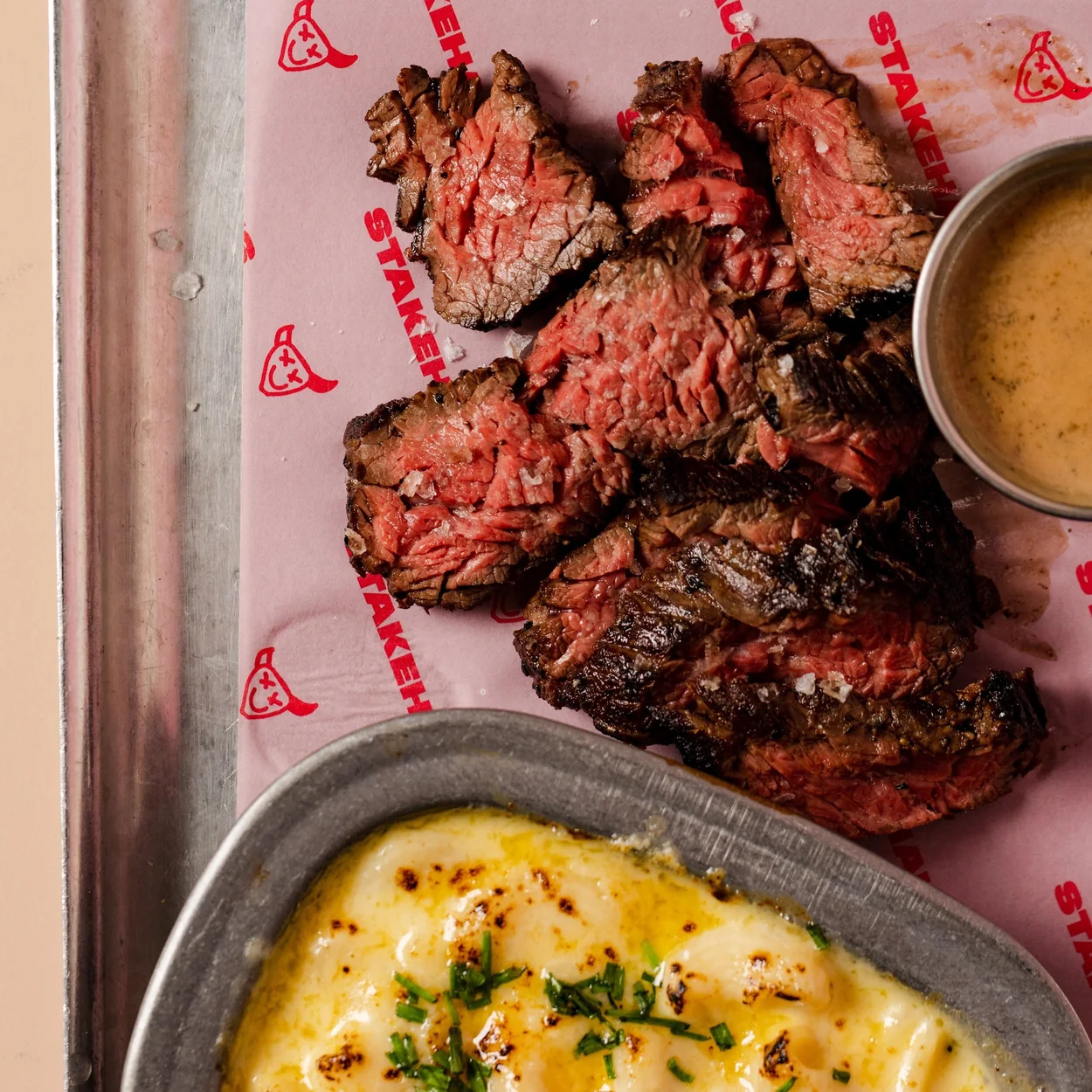 STAKEHAUS sliced steak on branded paper with a pot of sauce and a dish of macaroni cheese