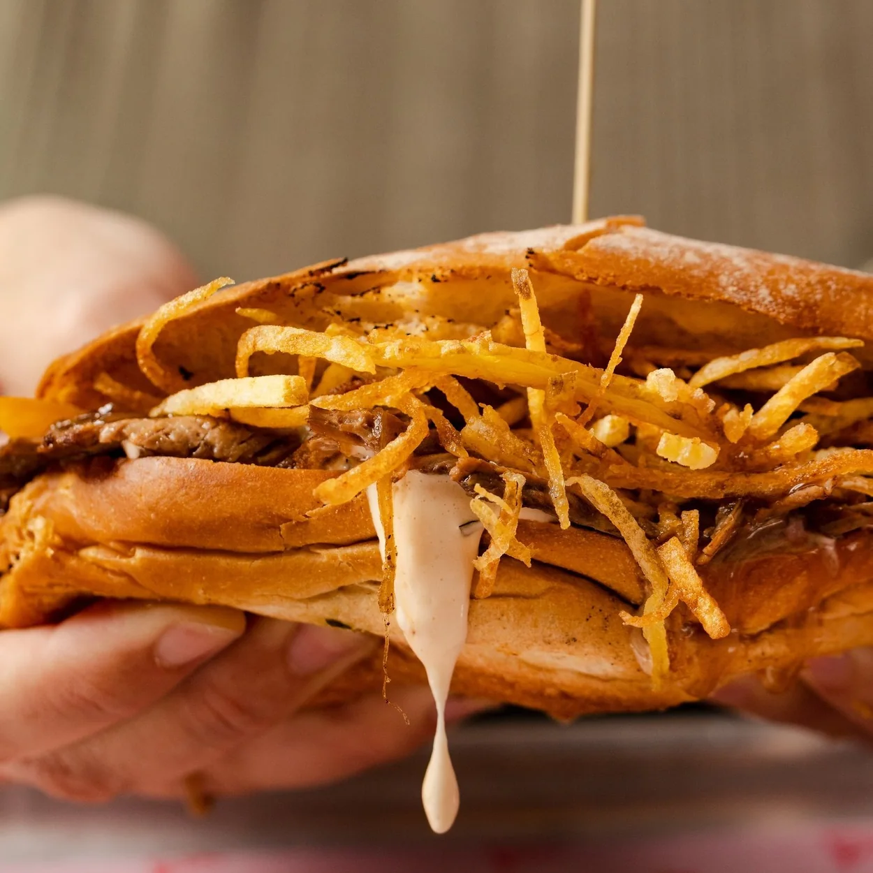 STAKEHAUS steak sandwich piled with fries and dripping sauce held in a hand