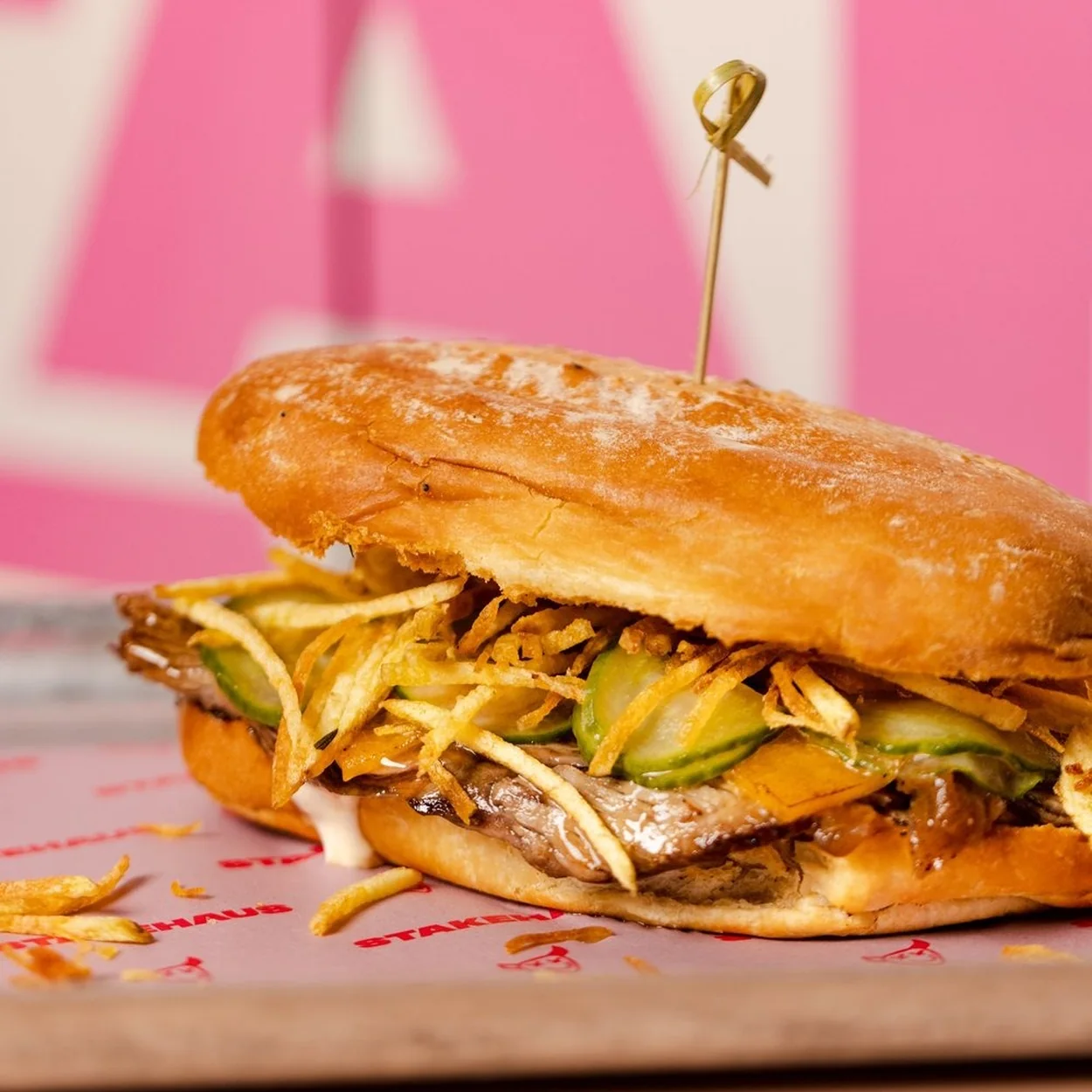 STAKEHAUS steak sandwich with pickles and cheese pinned with a skewer on a wooden board