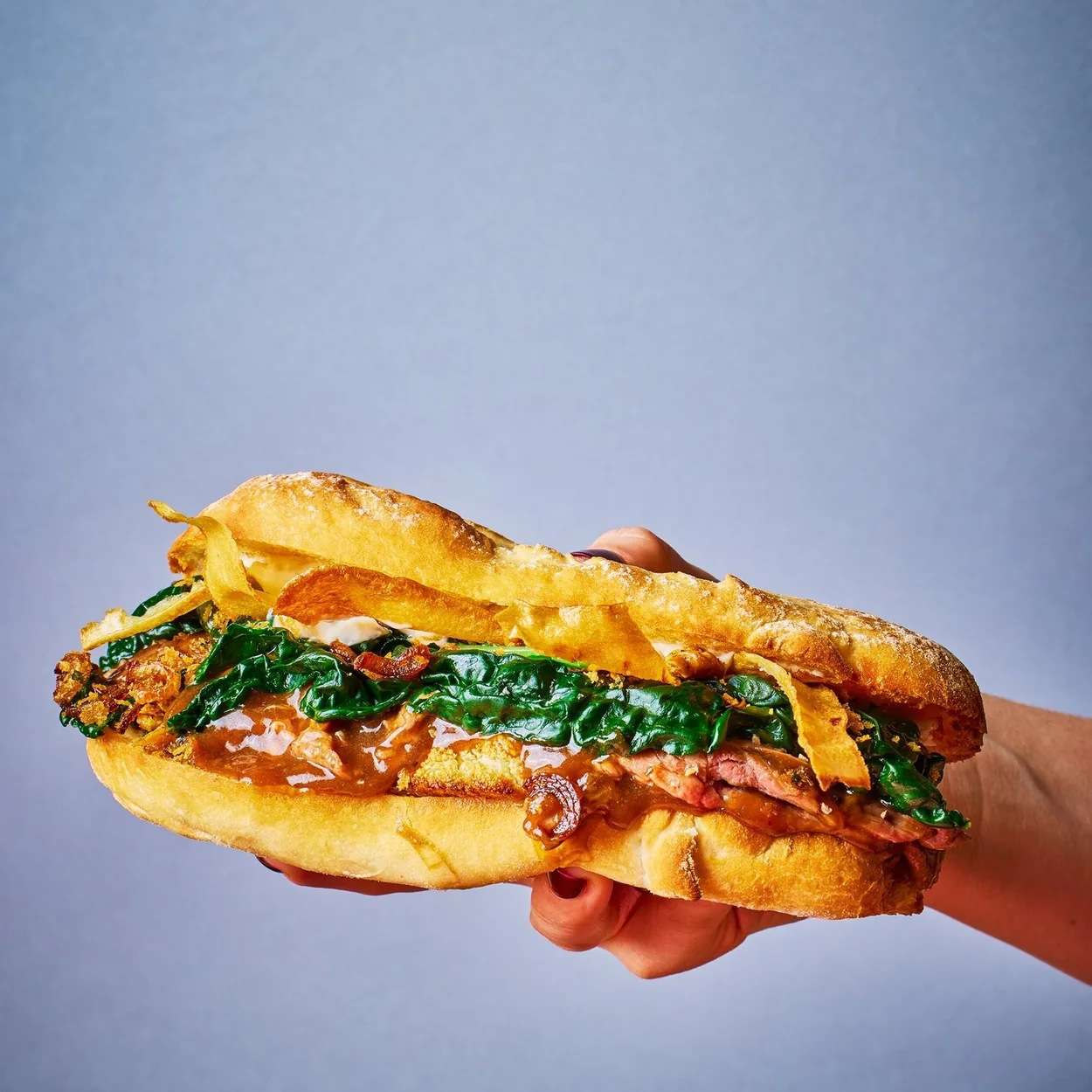 STAKEHAUS steak sandwich with greens held up against a plain blue background
